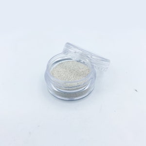 May include: A small clear plastic container with a lid, filled with a white glitter-like substance.