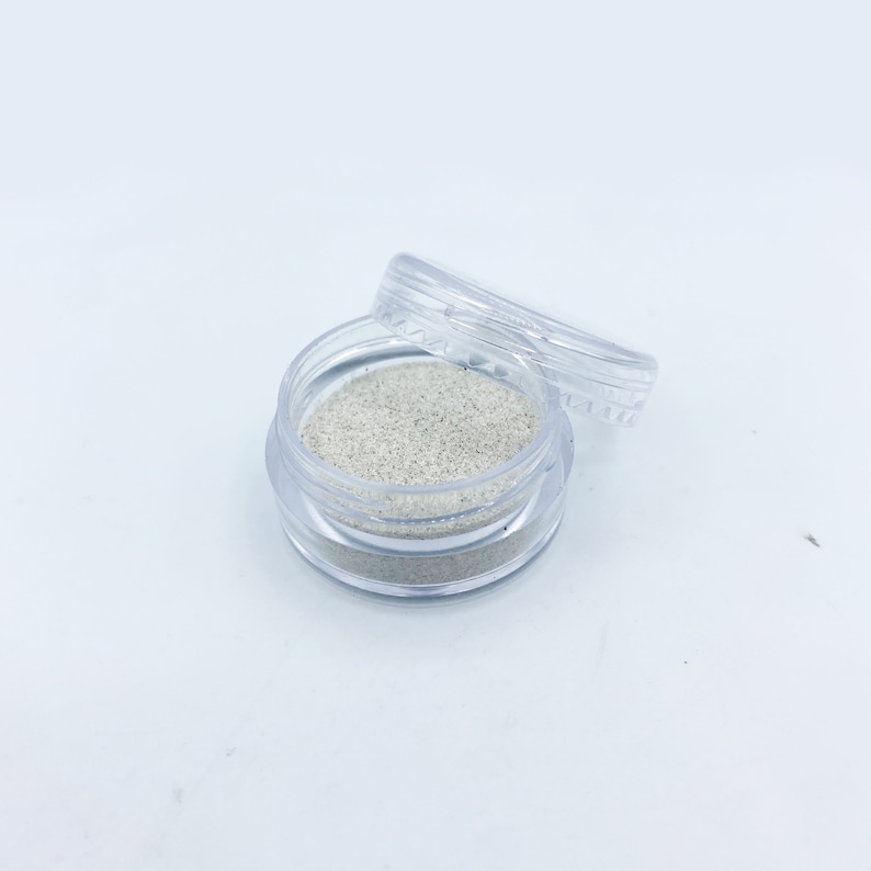May include: A small clear plastic container with a lid, filled with a white glitter-like substance.
