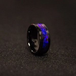Puede incluir: Un anillo de carburo de tungsteno negro con una incrustaci&oacute;n p&uacute;rpura y azul. El anillo tiene un acabado pulido y un ajuste c&oacute;modo.