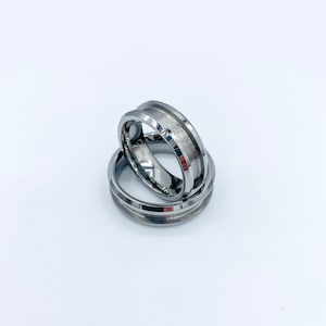 May include: Two silver tungsten carbide wedding bands with beveled edges. The bands are stacked on top of each other.