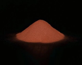 May include: A pile of reddish-brown powder on a black background.