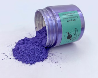 Puede incluir: Un tarro de polvo de mica púrpura etiquetado como "Astro Dust Premium Mica Powder 20 gramos Iris". El tarro está volcado y el polvo se derrama sobre una superficie blanca.