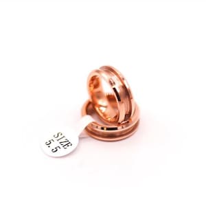 May include: Two rose gold wedding bands stacked on top of each other. The bands have a grooved design and are labelled "SIZE 5.5".