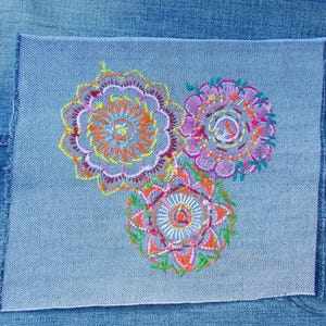 May include: A rectangular light blue denim patch featuring three circular embroidered mandala designs. The embroidery uses vibrant threads in shades of yellow, orange, pink, purple, and green, creating intricate patterns on the fabric surface.