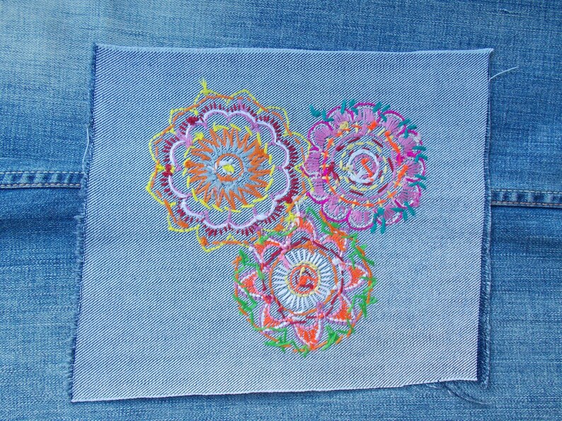 May include: A rectangular light blue denim patch featuring three circular embroidered mandala designs. The embroidery uses vibrant threads in shades of yellow, orange, pink, purple, and green, creating intricate patterns on the fabric surface.