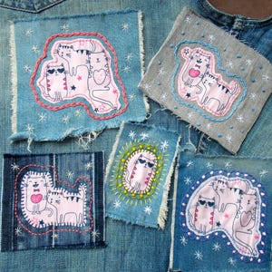 Op de afbeelding: Vijf rechthoekige denim stoffen patches met geborduurde kattenillustraties. De patches tonen diverse kattenontwerpen in roze, wit en zwart, geaccentueerd met handgestikte sterren, stippen en decoratieve randen in rood, blauw en geel garen.