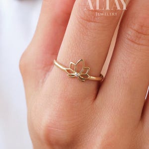 Op de afbeelding: Een gouden ring met een lotusbloem ontwerp. De ring heeft een dunne band en een gedetailleerde lotusbloem. De ring wordt aan een vinger gedragen. De merknaam "ALTAY JEWELLERY" is zichtbaar.