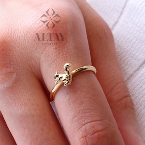 以下が含まれることがあります： リスのデザインの金の指輪。リスは右を向いていて、尻尾が丸まっています。