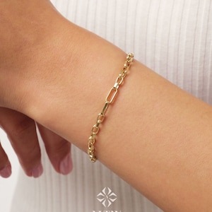 May include: A gold chain bracelet with a delicate, linked design. The bracelet is shown on a person's wrist.