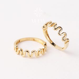 Peut inclure: Deux bagues dorées avec un motif ondulé. Les anneaux sont en métal jaune brillant et se détachent sur un fond blanc. Le design ondulé unique ajoute une touche de modernité à ces bijoux, parfaits pour toutes les occasions.