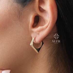 May include: Gold square hoop earrings with a textured design. The earrings are shown on a model's ear.