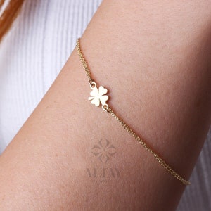 Puede incluir: Una pulsera dorada con un dije de tr&eacute;bol de cuatro hojas. La delicada pulsera de cadena se lleva en el brazo. El dije de tr&eacute;bol est&aacute; centrado en la pulsera. La marca "ALTAY" es visible en la esquina inferior derecha.