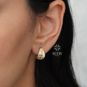 May include: A close-up of a person's ear wearing a gold hoop earring. The earring is a simple, smooth, and slightly curved design. The text "ALTAW JEWELLERY" is visible in the lower right corner of the image.