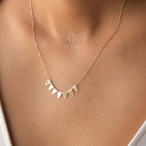 Puede incluir: Un collar de oro con una cadena delicada y un colgante hecho de siete pequeñas formas triangulares. El colgante está dispuesto en una línea curva, creando un aspecto moderno y minimalista.