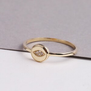 May include: A gold ring with a round, textured bezel set with small clear stones in the shape of an eye.