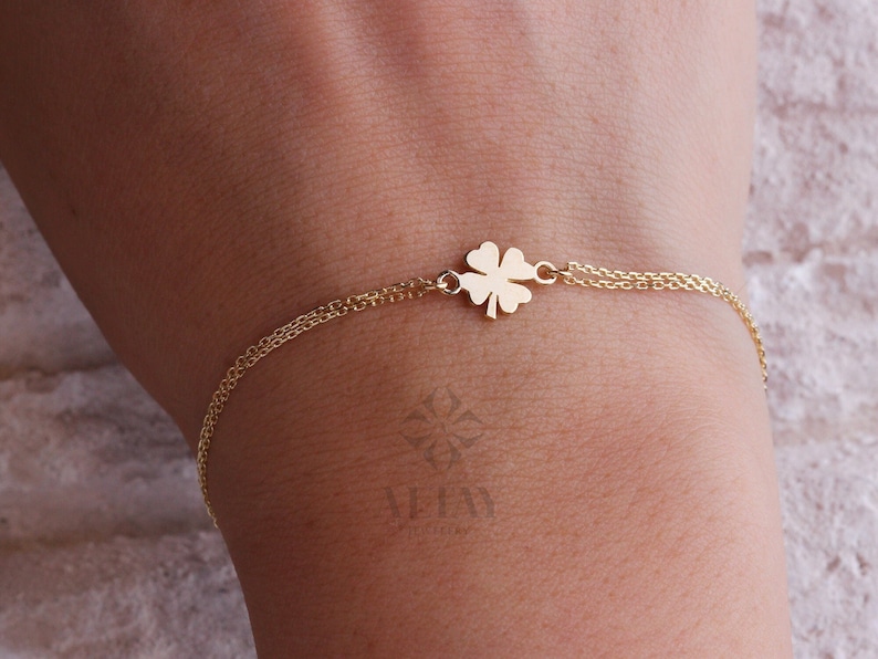 Puede incluir: Una pulsera dorada con un dije de tr&eacute;bol de cuatro hojas. El dije est&aacute; conectado a una fina cadena doble. La pulsera se muestra en una mu&ntilde;eca, resaltando el dise&ntilde;o y el color. El tr&eacute;bol es un s&iacute;mbolo de buena suerte.