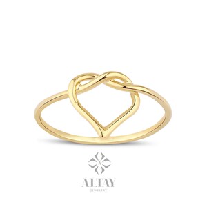 May include: A gold ring with a heart-shaped design. The heart is formed by two intertwined loops of metal.