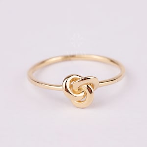May include: A gold knot ring with a simple design. The ring is made of a smooth, polished metal and has a delicate knot shape.