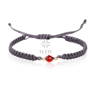 May include: Grey braided cord bracelet with a gold ladybug charm. The ladybug has red wings and black spots.