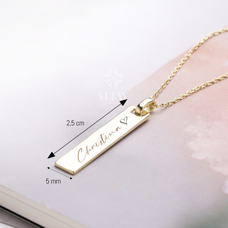 May include: Gold necklace with a personalized bar pendant engraved with the name "Christina" and a small heart symbol. The pendant is 2.5 cm long and 0.5 cm wide.