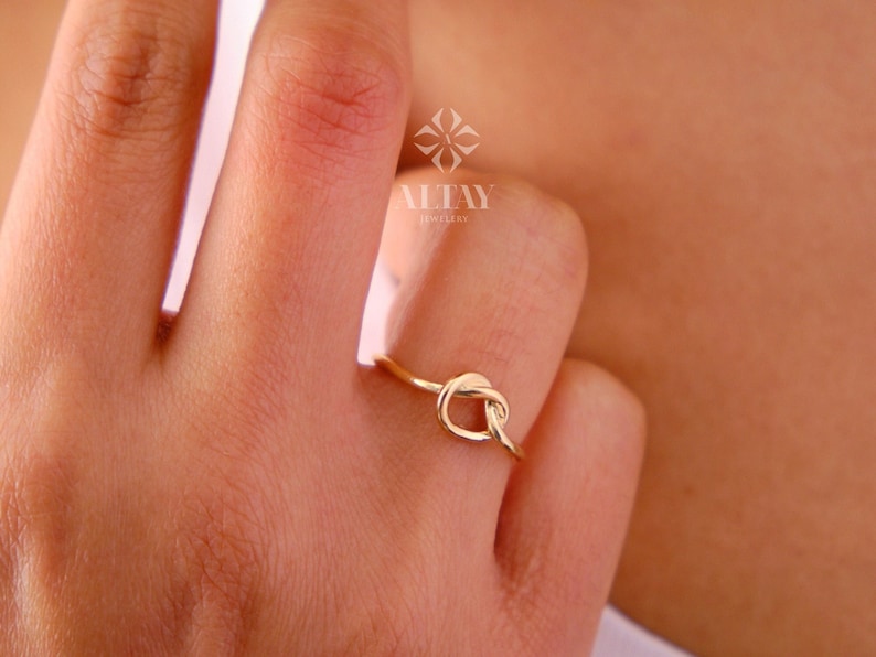 Op de afbeelding: Een gouden knoop ring aan een vinger. De ring is een eenvoudig ontwerp met een knoopvorm. De ring wordt gedragen aan de ringvinger van een hand.