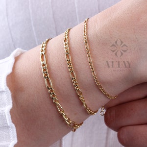 May include: Three gold chain bracelets on a person's wrist. The bracelets are different widths and have a classic chain design.