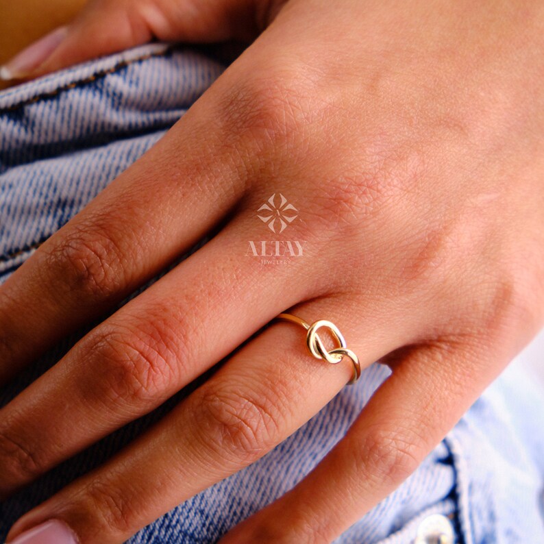 Op de afbeelding: Een gouden knoop ring aan een vinger. De ring is simpel en elegant, met een gladde afwerking.