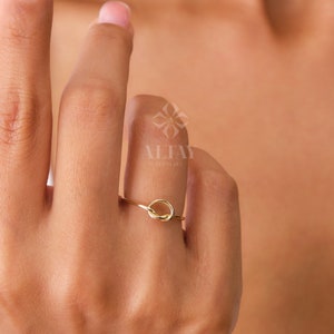 Op de afbeelding: Een eenvoudige gouden ring met een knoopdesign. De ring zit aan een vinger.
