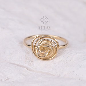 Puede incluir: Un anillo de oro con un diseño en forma de rosa. El anillo está hecho de una sola pieza de alambre que se tuerce y gira para crear la forma de la rosa. El anillo es simple y elegante.