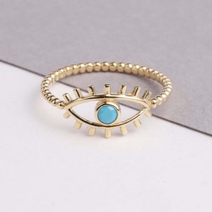 May include: A gold ring with a blue evil eye charm. The ring is made of a twisted band of gold.