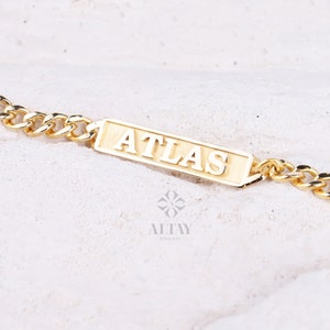Pode incluir: Um bracelete de corrente de ouro com uma placa retangular que diz "ATLAS" em letras em relevo.