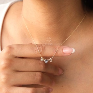 Può includere: Una collana d'oro con tre ciondoli a forma di cuore. I cuori sono di dimensioni diverse e sono disposti in fila.