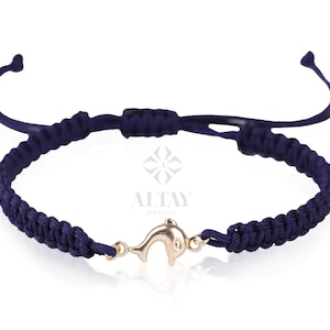 Puede incluir: Un brazalete de cordón trenzado azul marino con un dije de delfín dorado.