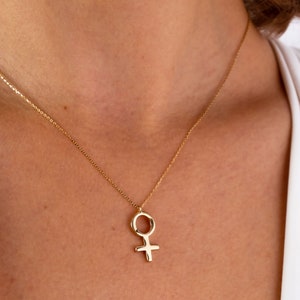 K&ouml;nnte beinhalten: Eine goldene Halskette mit einem schlichten, minimalistischen Anh&auml;nger in Form des weiblichen Symbols.
