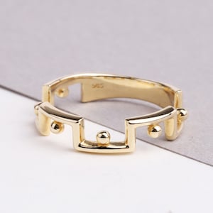 May include: A gold ring with a geometric design featuring a series of connected squares and circles.