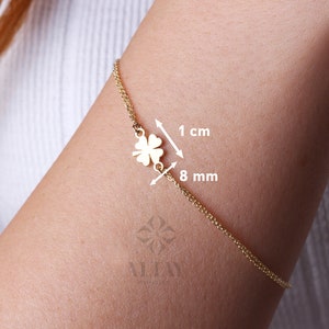Puede incluir: Una pulsera dorada con un colgante de tr&eacute;bol de cuatro hojas. El dije mide aproximadamente 1 cm de ancho. La pulsera se muestra en el brazo de una persona.