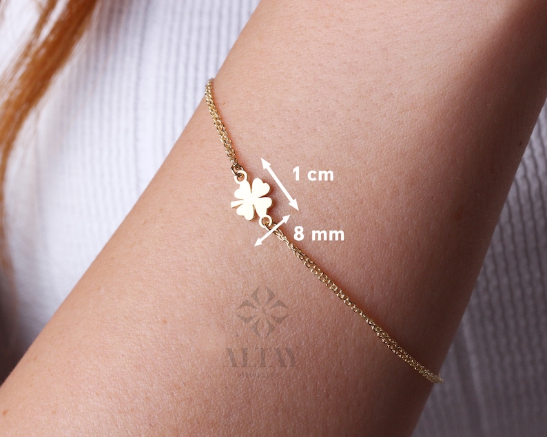 Puede incluir: Una pulsera dorada con un colgante de tr&eacute;bol de cuatro hojas. El dije mide aproximadamente 1 cm de ancho. La pulsera se muestra en el brazo de una persona.