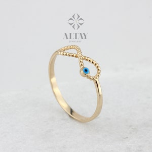 May include: Gold infinity ring with a blue evil eye charm. The ring is made of beaded gold and has a delicate design.