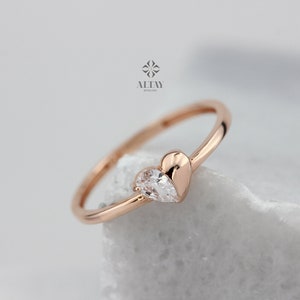 May include: A rose gold ring with a pear-shaped clear stone set in a heart-shaped design.