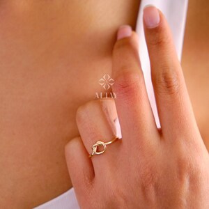 Op de afbeelding: Een gouden knoop ring aan een vinger. De ring is simpel en elegant, met een gladde afwerking. De ring is gemaakt van 14 karaat goud en is verkrijgbaar in verschillende maten.
