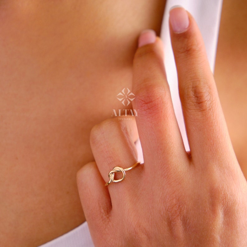 Op de afbeelding: Een gouden knoop ring aan een vinger. De ring is simpel en elegant, met een gladde afwerking. De ring is gemaakt van 14 karaat goud en is verkrijgbaar in verschillende maten.