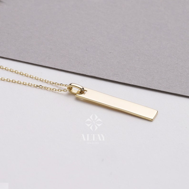 May include: A gold bar pendant necklace with a delicate chain. The pendant is a simple, rectangular shape.