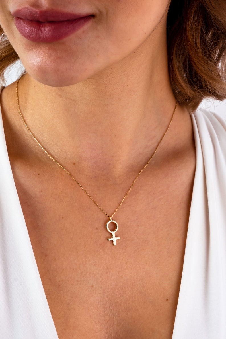 K&ouml;nnte beinhalten: Eine goldene Halskette mit einer zarten Kette und einem Anh&auml;nger in Form des weiblichen Symbols.