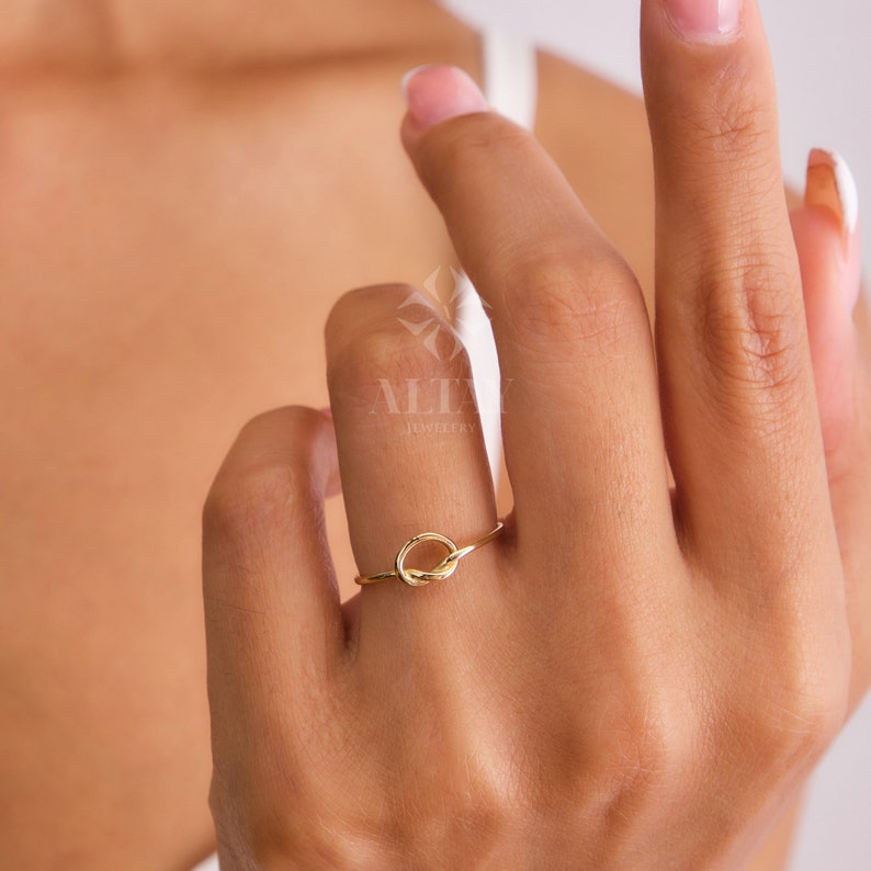 Op de afbeelding: Een gouden knoop ring met een eenvoudig, elegant ontwerp. De ring wordt gedragen aan de vinger van een persoon.