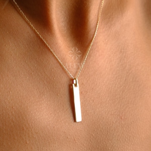May include: A gold chain necklace with a long, rectangular pendant.
