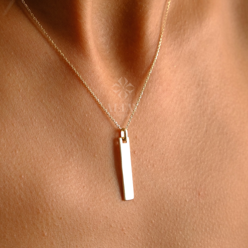 May include: A gold chain necklace with a long, rectangular pendant.
