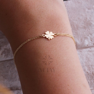 Puede incluir: Una pulsera dorada con un dije de tr&eacute;bol de cuatro hojas. La delicada pulsera de cadena se muestra en un brazo. El dije de tr&eacute;bol es el centro de atenci&oacute;n. Una joya sencilla y elegante.