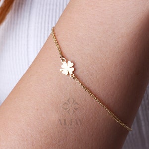 Puede incluir: Una delicada pulsera dorada con un dije de tr&eacute;bol de cuatro hojas. La pulsera es un dise&ntilde;o de cadena fina, con el dije de tr&eacute;bol centrado. La pulsera se lleva en el brazo de una persona, mostrando la elegante simplicidad de la joya.