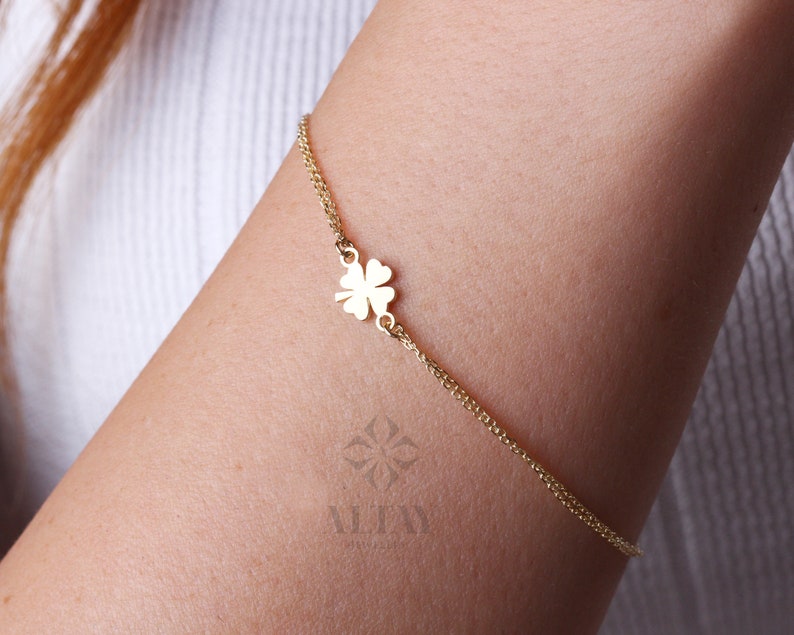 Puede incluir: Una delicada pulsera dorada con un dije de tr&eacute;bol de cuatro hojas. La pulsera es un dise&ntilde;o de cadena fina, con el dije de tr&eacute;bol centrado. La pulsera se lleva en el brazo de una persona, mostrando la elegante simplicidad de la joya.