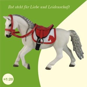 Ein weißes Schleich Pferd mit einem Sattel und einer Trense in Rot.